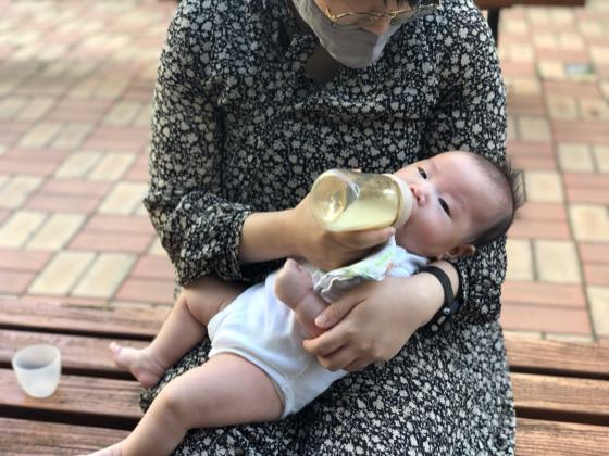 야외 벤치에서 아기를 안고 젖병으로 수유하는 모습
