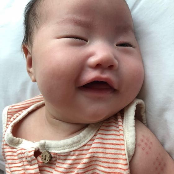 Close-up of a baby in striped clothes, eyes closed, beaming — a daily shot that, placed beside your line, brings back the day's expression whole