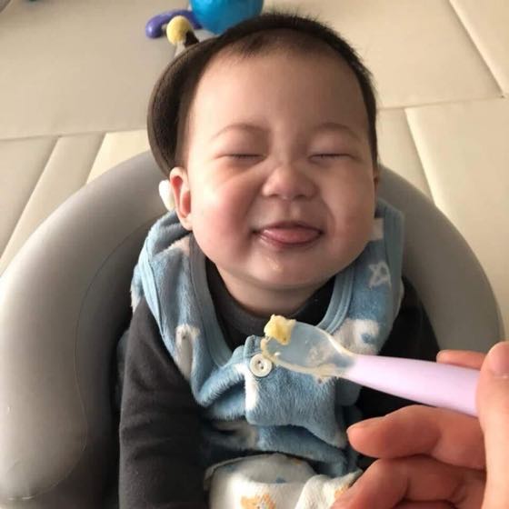 A baby in a bib beaming while taking a first spoonful of solids