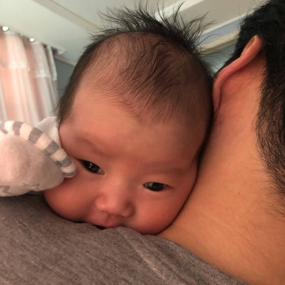 親の肩にもたれて抱かれ、カメラを見つめる赤ちゃん