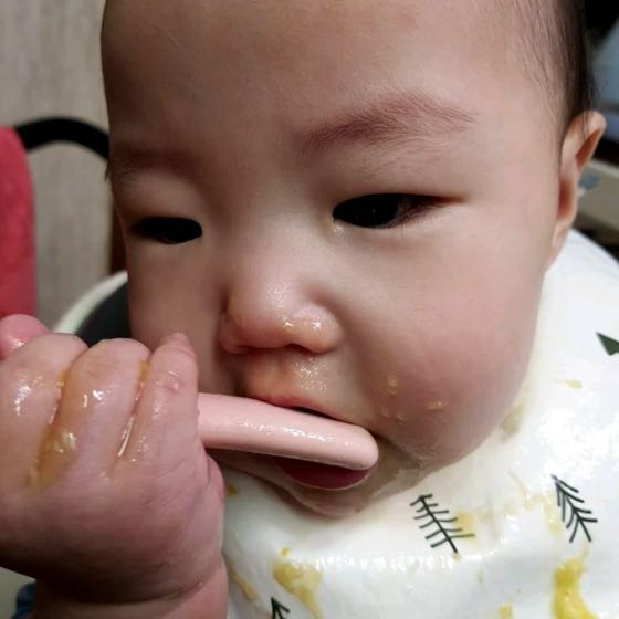 아기 의자에 앉아 숟가락으로 이유식을 받아먹는 아기