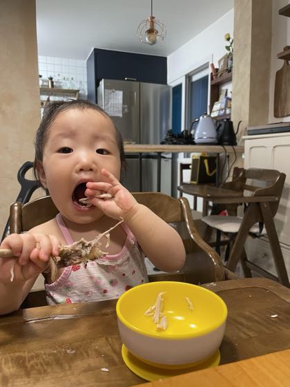A baby past age 1 at the table with a bowl, picking up food to self-feed