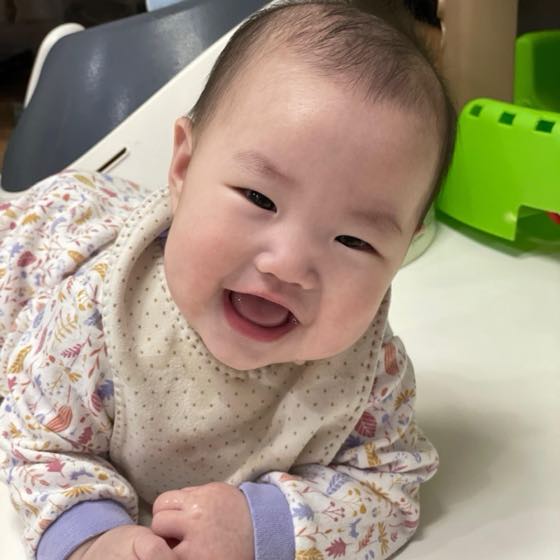 A healthy baby sitting in a high chair, smiling brightly
