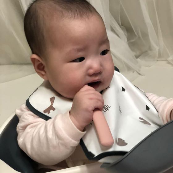 A baby holding a soft one-piece teether with both hands and chewing on it