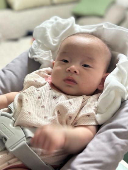 ベビーチェアにもたれてカメラを見つめる2〜3か月の赤ちゃん