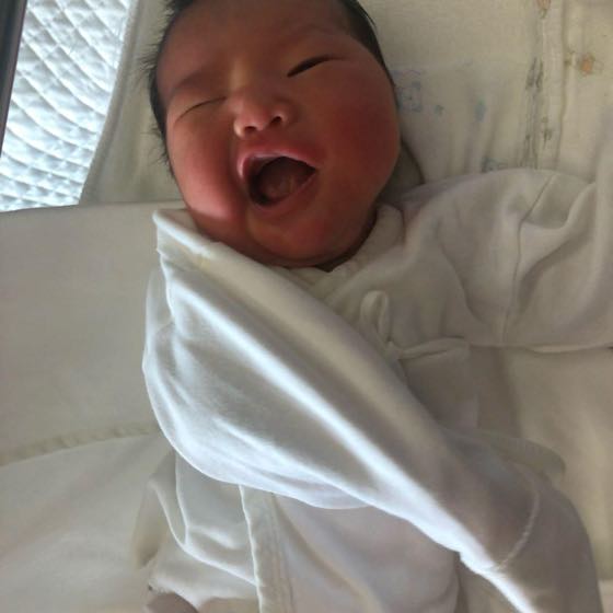 白いおくるみに包まれ、目を覚ましてあくびをする新生児
