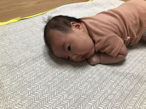 床のマットにうつ伏せで寝そべる新生児(タミータイム)